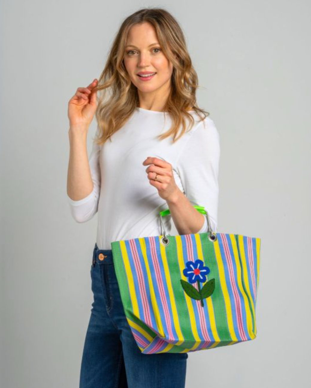 Woman holding a colorful striped tote bag with a floral design on a gray background